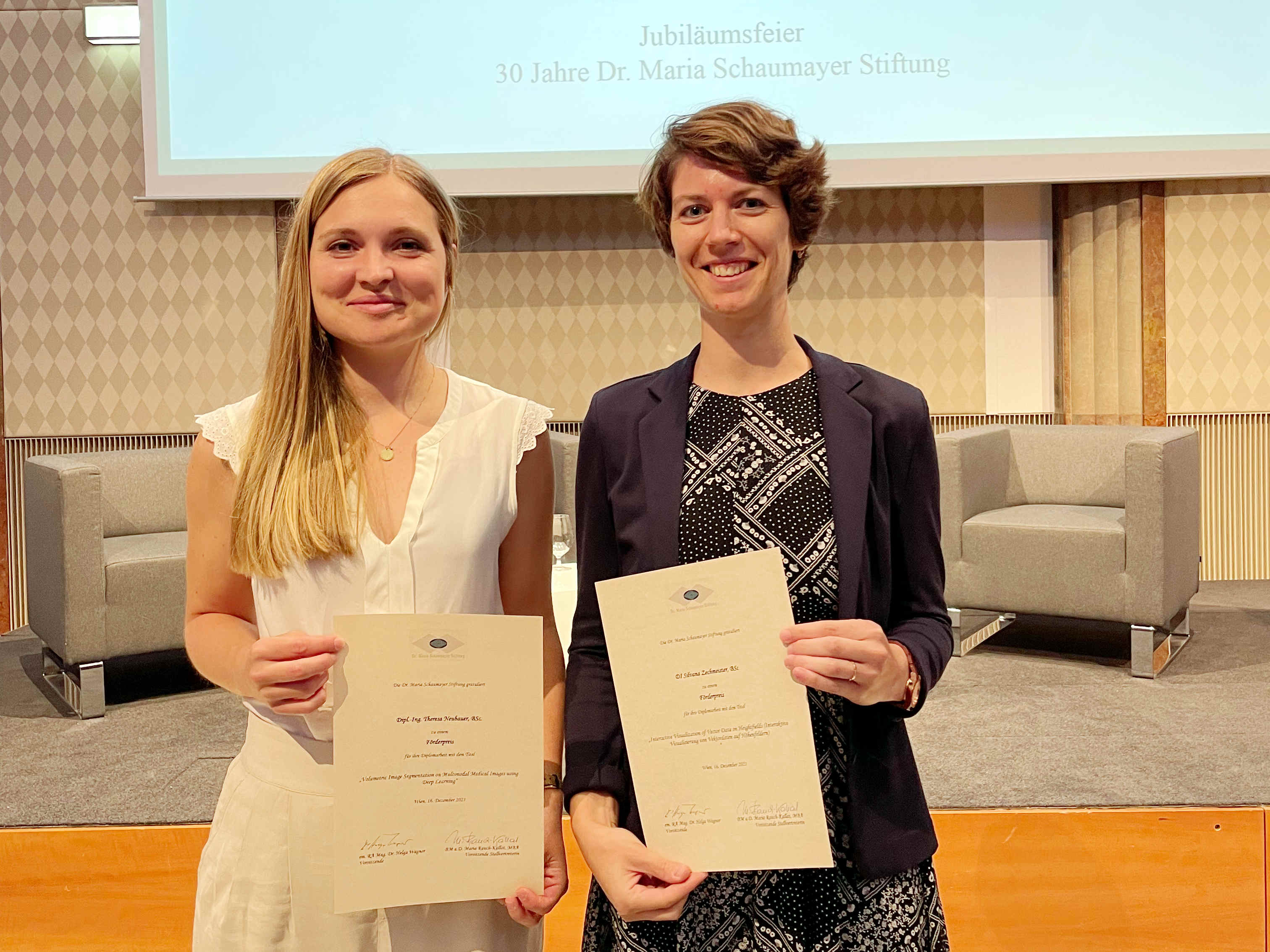 Two female researchers hold award certificates. 