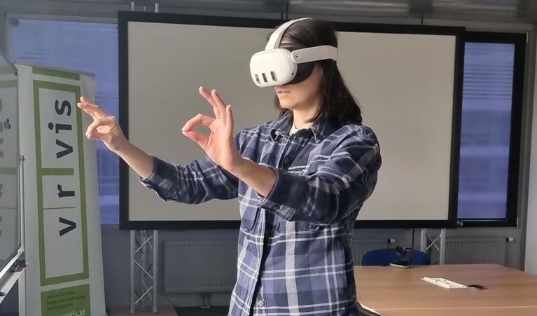 Eine Frau trägt eine Quest-VR-Brille und macht dazu Handgesten, im Hintergrund ist ein VRVis-Banner zu sehen.