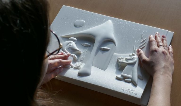 View from above: a woman with glasses is touching a tactile relief with her hands.