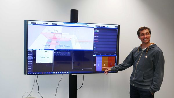 A researcher in front of a large screen points to the lower right corner of the screen.