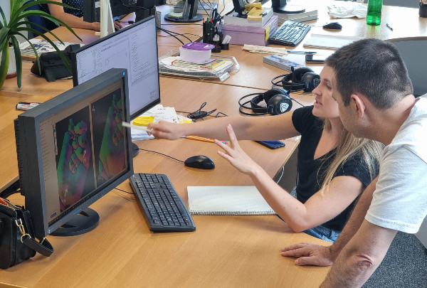 Forscherin Theresa Neubauer zeigt auf einen Computerbildschirm auf dem ihre Forschungsarbeit zu Künstlicher Intelligenz zu sehen ist. Ein Mann hört aufmerksam zu.