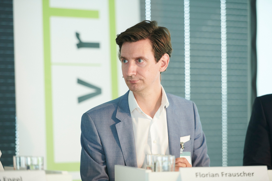 Florian Frauscher sits on the podium of a panel discussion, the VRVis logo can be seen in the background.