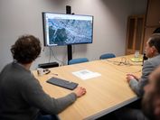 People look at a large monitor showing a 3D representation of a city neighborhood. 