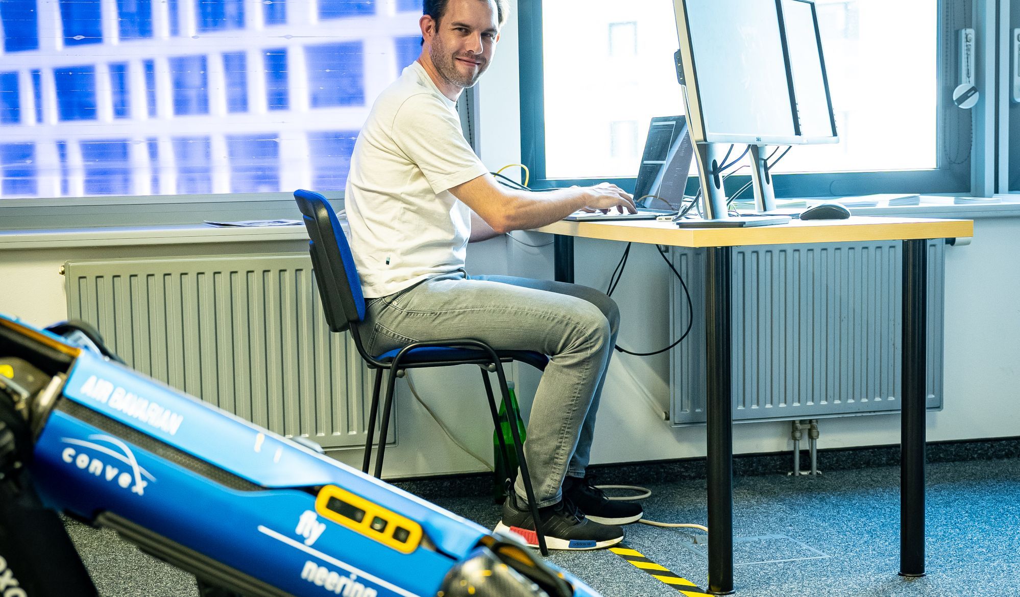 Ein Mann sitzt an einem Computer, neben ihm steht ein Laufroboter