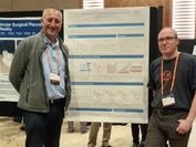 Two men stand in front of a scientific poster at a scientific conference.