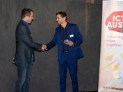 Two men in suits shake hands at an awards ceremony.