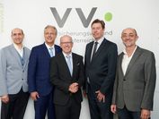 Five gentlemen in suits stand in front of a VVO banner.