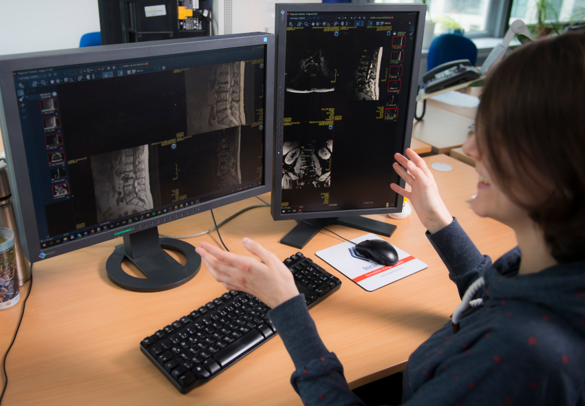 A VRVis researcher shows two computer screens on which spinal scans can be seen.