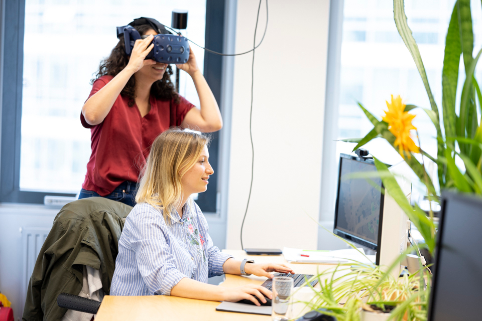 Zwei Forscherinnen sitzen vor einem Desktop-Computer. Eine von ihnen hat ein VR-Headset auf.