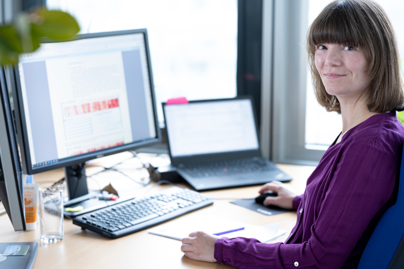 Milena Vuckovic, Forscherin des VRVis, sitzt vor einem Desktop Computer und lächelt in die Kamera, auf dem Bildschirm sind Klimadatenvisualisierungen zu sehen.
