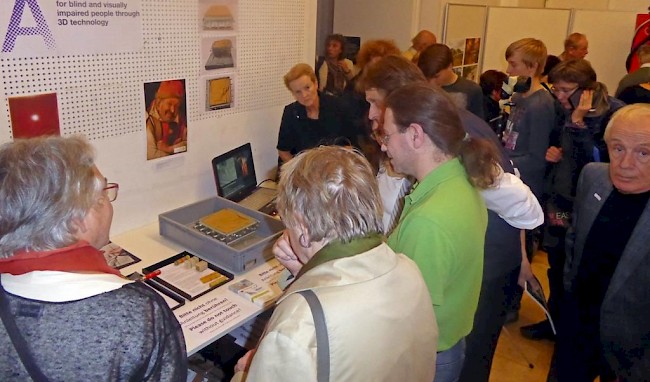 Viele Menschen sind bei einer Ausstellung, wo sie den Nudeldrucker anschauen und angreifen können.