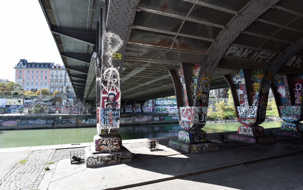 Bridge pier at the Donaukanal, covered with graffiti, the river flows in the background