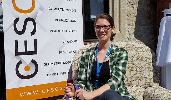 Silvana Zechmeister, student at VRVis, sitting in the sun in front of the logo of the CESCG 2018