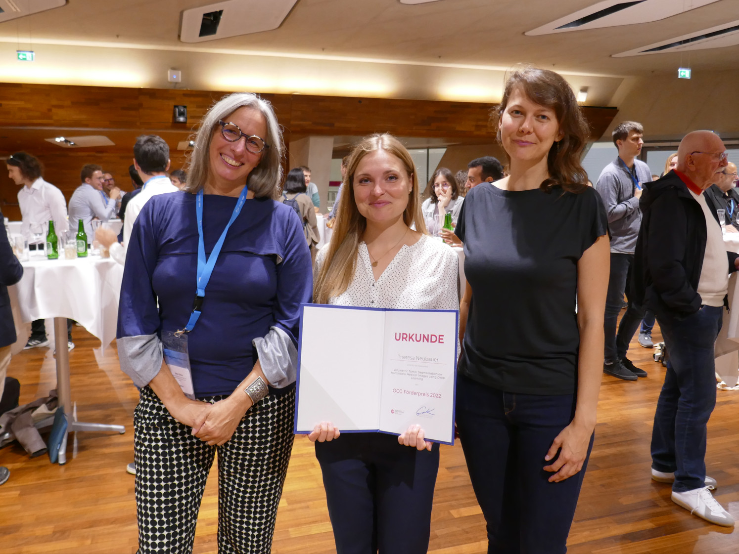 Drei Forscherinnen, die Forscherin in der Mitte hält die Urkunde des OCG Förderpreis 2022. 