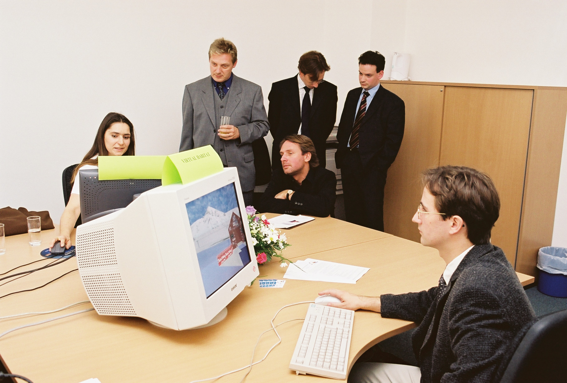 Ein Mann und eine Frau sitzen vor je einem altmodischen Computerbildschirm, auf welchen Visualisierungen zu sehen sind und zeigen Gästen eine Demo.