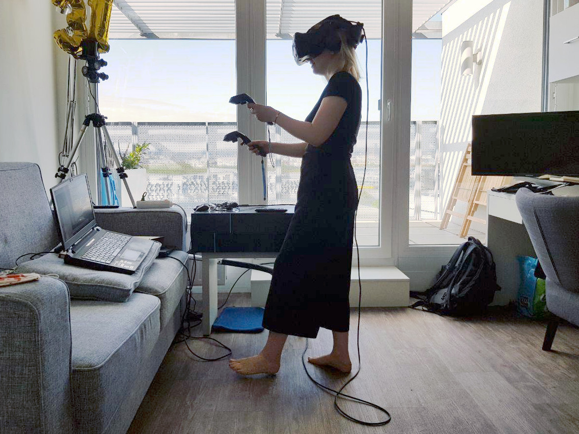 Eine Forscherin in ihrem Wohnzimmer mit einer VR-Brille und Controllern. 