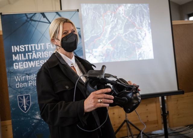 Eine Frau mit Mund-Nasen-Schutz hält eine VR-Brille in der Hand.