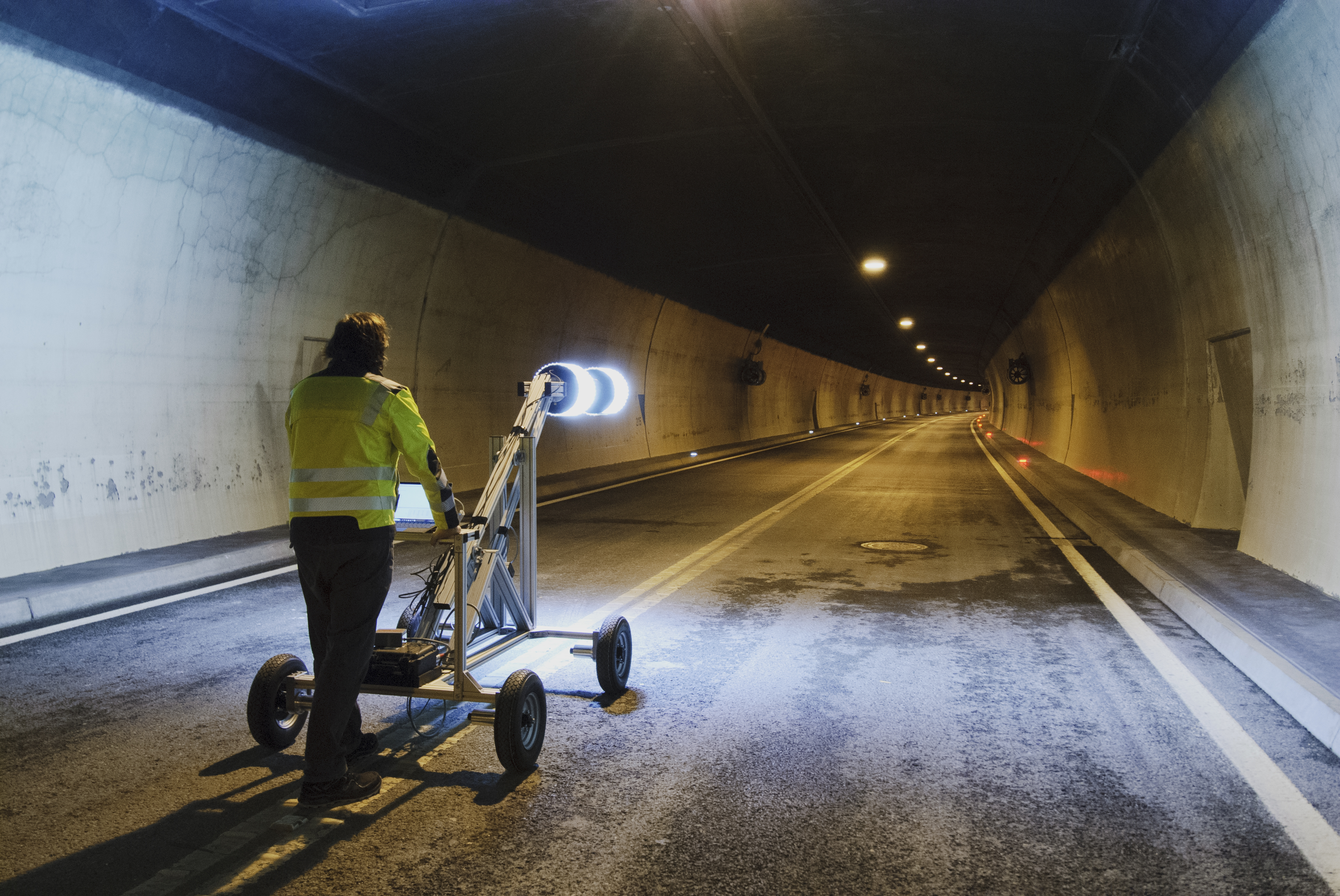A man stands in a tunnel with a tunnel surveyor that lights up to survey the tunnel for cracks. 