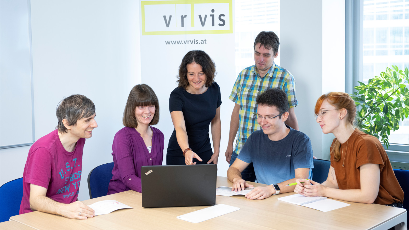 Das Team "Visual Analytics" des VRVis an einem Besprechungstisch mit Laptop und VRVis-Banner im Hintergrund. 