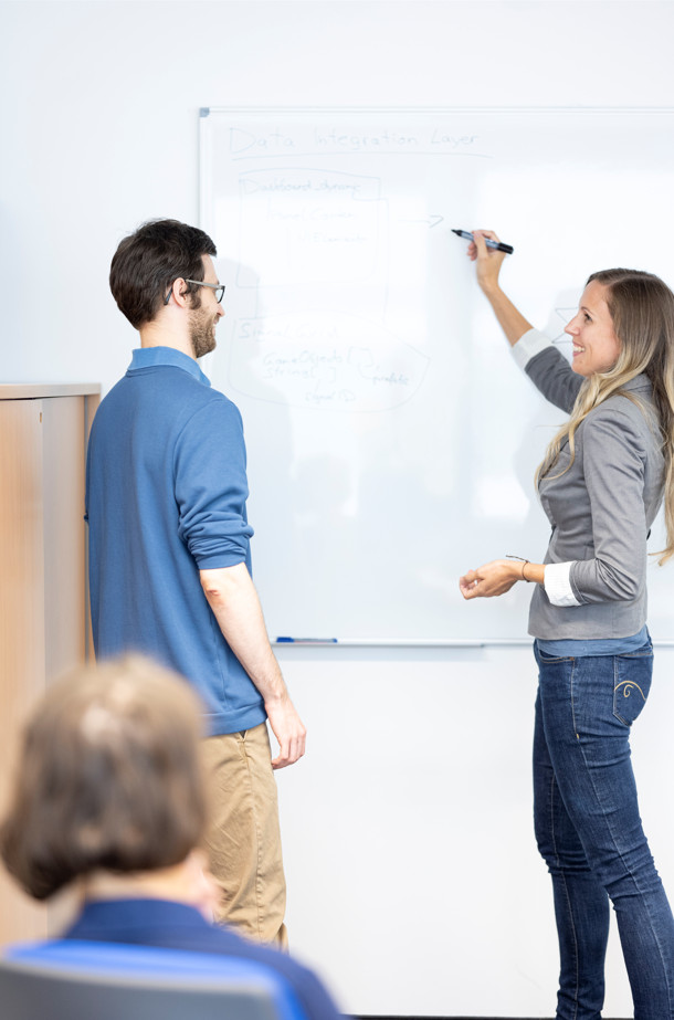 Ein Forscher und eine Forscherin stehen im Gespräch vor einem Whiteboard.