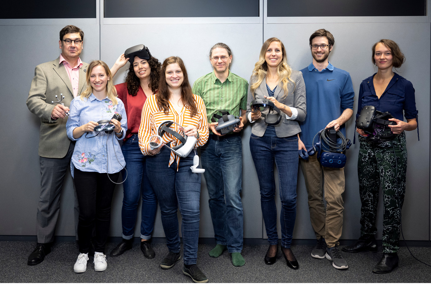 Eight researchers holding different virtual reality goggles in their hands. 