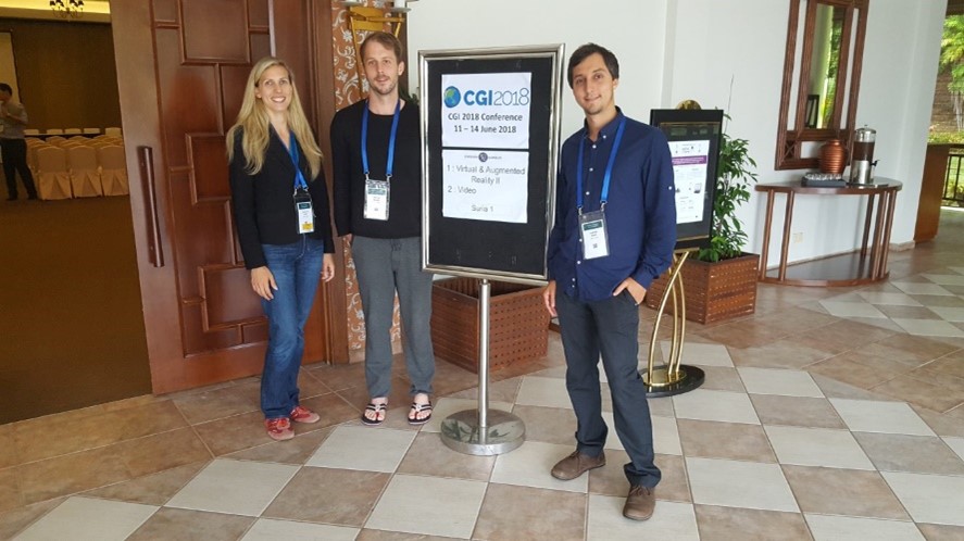 Three researchers stand around a sign next to an entrance door. 