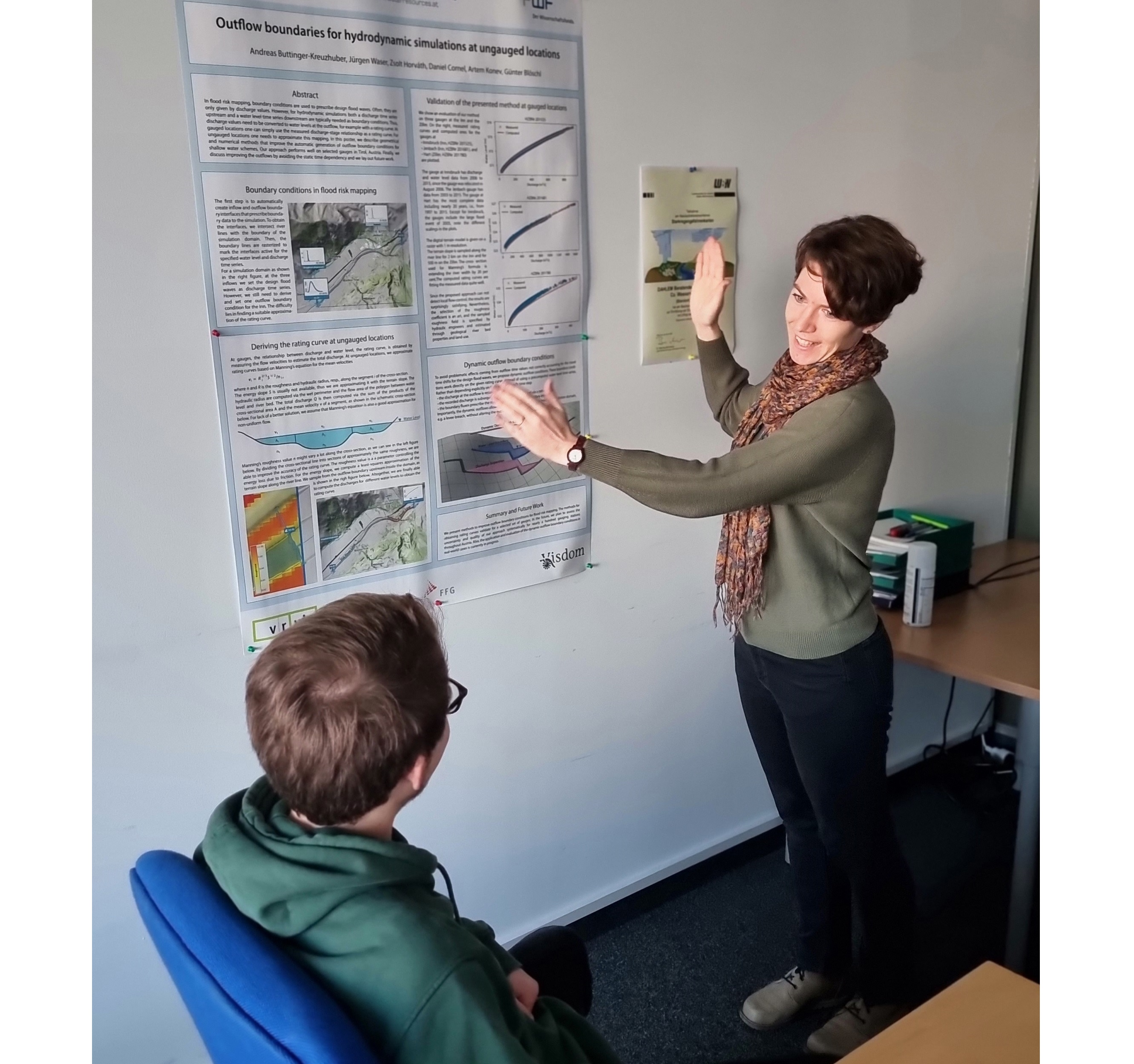 A researcher is standing in front of a scientific poster explaining something to a fellow researcher.