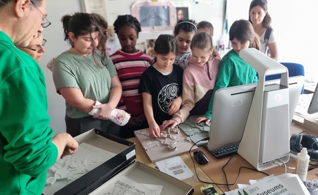 A group of girls stands close together and touches a tactile relief that VRVis researcher Andreas Reichinger is showing at Daughters' Day.