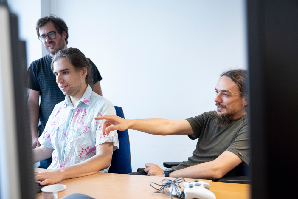 Drei Forscher vor Bildschirmen, der ganz rechts deutet auf einen Monitor. 