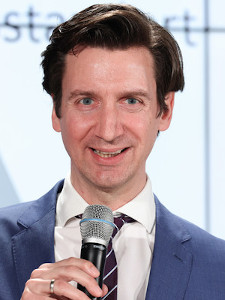 Portrait photo of Florian Frauscher, who is holding a microphone in his hand. 