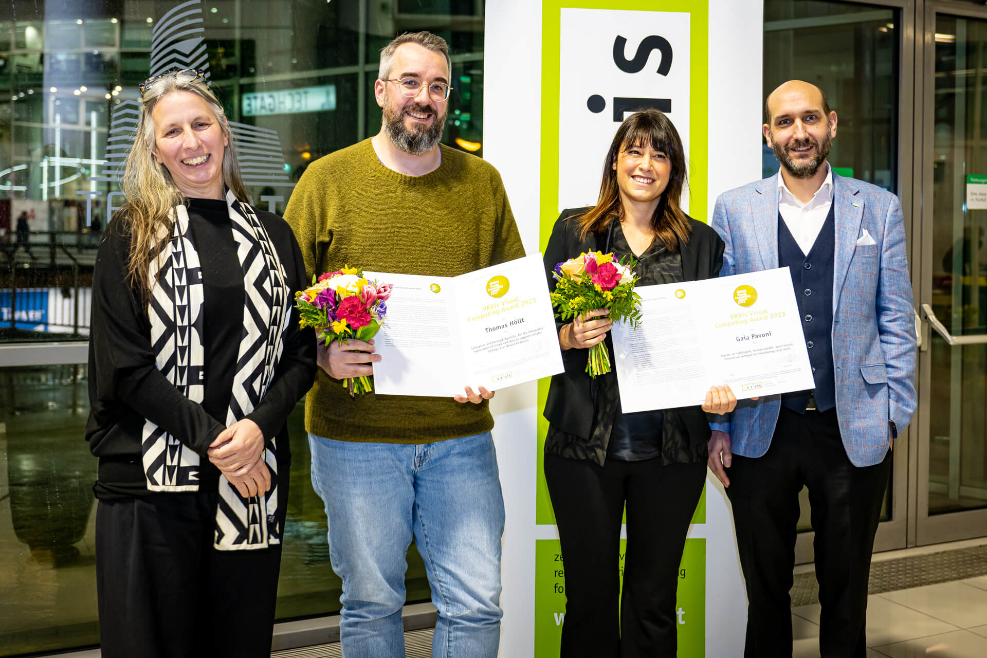 Two award winners with flowers and award certificate in the middle, on the right and on the left the scientific and management of VRVis