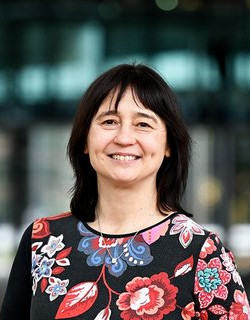 A woman with long dark hair, she is wearing a shirt with flowers in various colours