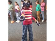 Ein Mädchen mit aufgesetzter VR-Brille zeigt mit einem VR-Controller Richtung Kamera, im Hintergrund sind unscharf weitere Mädchen zu sehen.