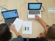 Zwei Frauen sitzen vor zwei Laptops und präsentieren eine wissenschaftliche Präsentation in einer Online-Konferenz.