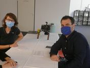 Eine Forscherin und ein Forscher sitzen mit Mundschutz an einem Tisch. 