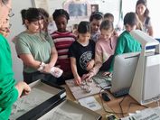 A group of girls stands close together and touches a tactile relief that VRVis researcher Andreas Reichinger is showing at Daughters' Day.