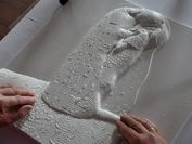 Ein taktiles Relief von Gustavs Klimt "Der Kuss", welches von zwei Händen berührt wird. 