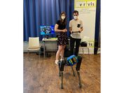 Eine Forscherin und ein Forscher mit einem blauen Roboterhund. 