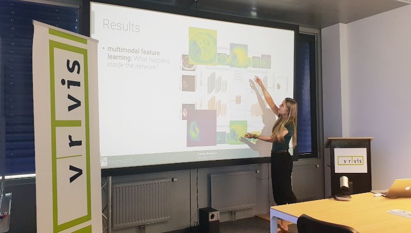 A female researcher stands in front of a presentation wall and presents the results of her deep learning based research work.