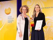 Das Logo des Liese-Prokop-Frauenpreises auf gelbem Hintergrund links, rechts daneben stehen zwei Frauen.
