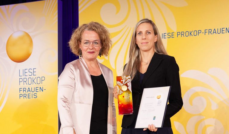 The logo of the Liese Prokop Women's Award on a yellow background on the left, with two women standing to the right.