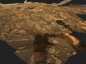 Zu sehen ist eine lose Gesteinsformation aus einer Rekonstruktion der Marsoberfläche in braunen Farben sowie der Schatten des Mars-Rovers Perseverance, welcher die Aufnahmen getätigt hat.