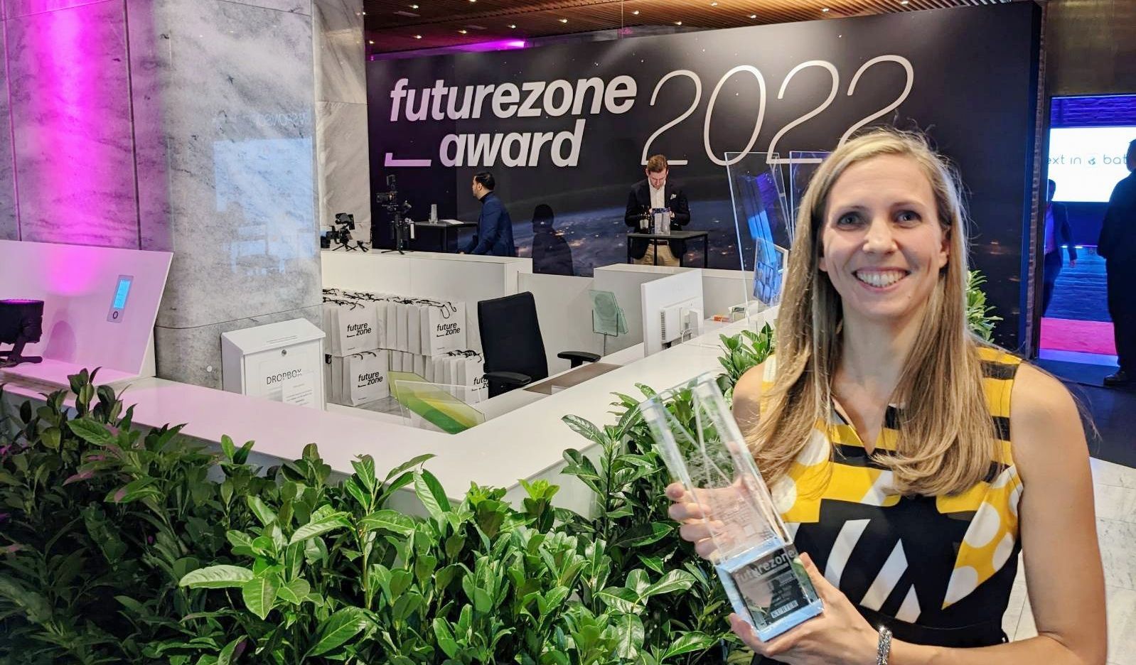 Am rechten Bildrand steht eine Frau, die eine Glastrophäe hält. Im Hintergrund der Schriftzug "Futurezone Awards 2022"