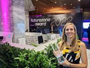 On the right edge of the picture is a woman holding a glass trophy. In the background the lettering "Futurezone Awards 2022".