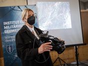 Eine Frau mit Mund-Nasen-Schutz hält eine VR-Brille in der Hand.