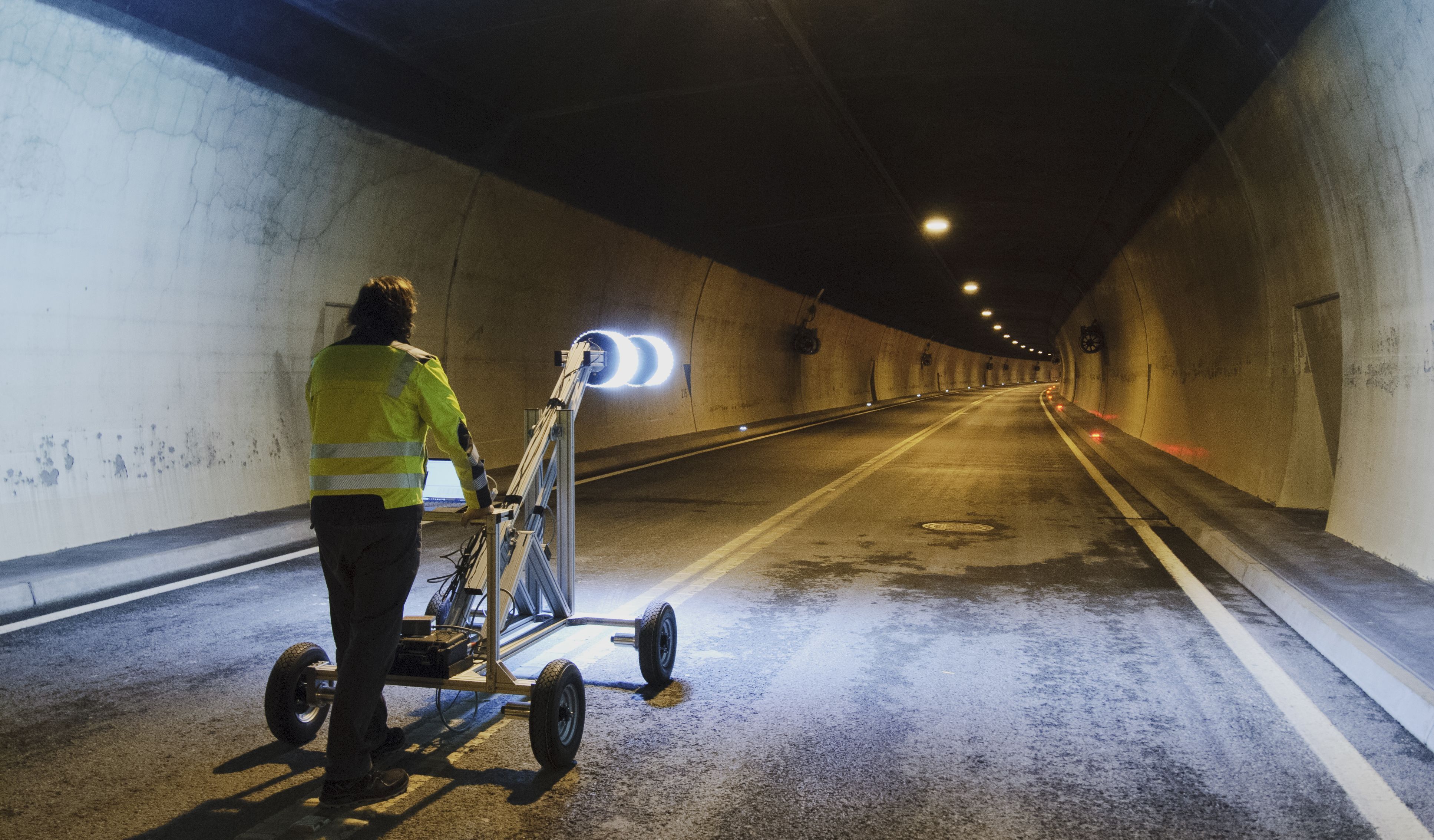 Ein Mann steht mit einem Tunnelvermessungsgerät, das leuchtet, in einem Tunnel, um diesen zu vermessen.
