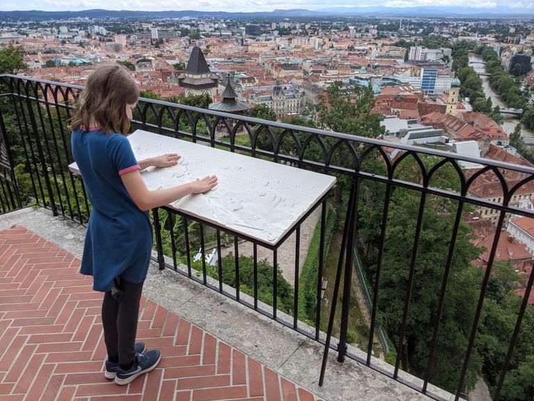 Ein Mädchen steht vor dem taktilen Panoramarelief und berührt es mit den Händen.