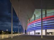 Teil eines Fußballstadions mit hohen Glasfenstern und rot-blauer Beleuchtung