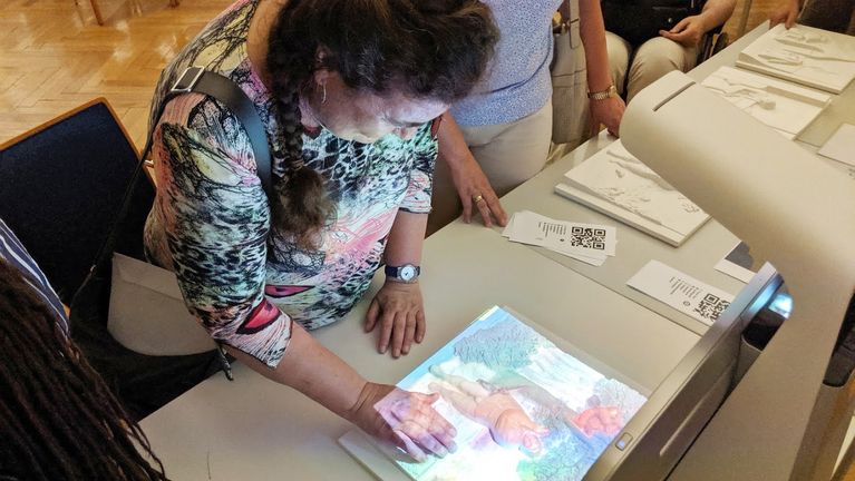 An elderly lady touches a relief colored with light with her hand. 